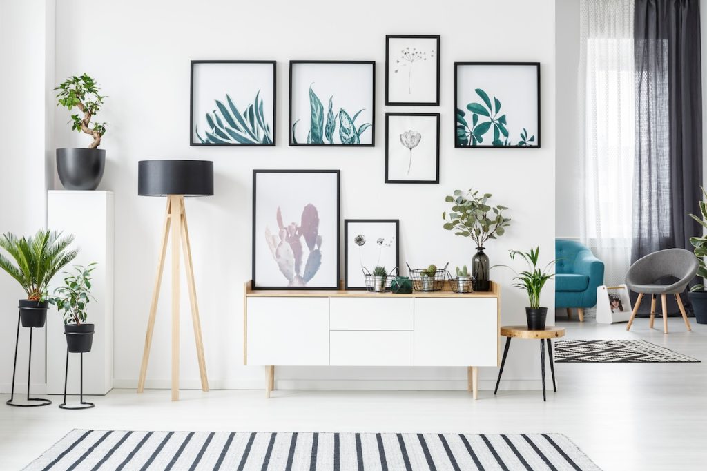 Botanical posters on the wall in a living room interior with white cabinet, wooden lamp and plants
