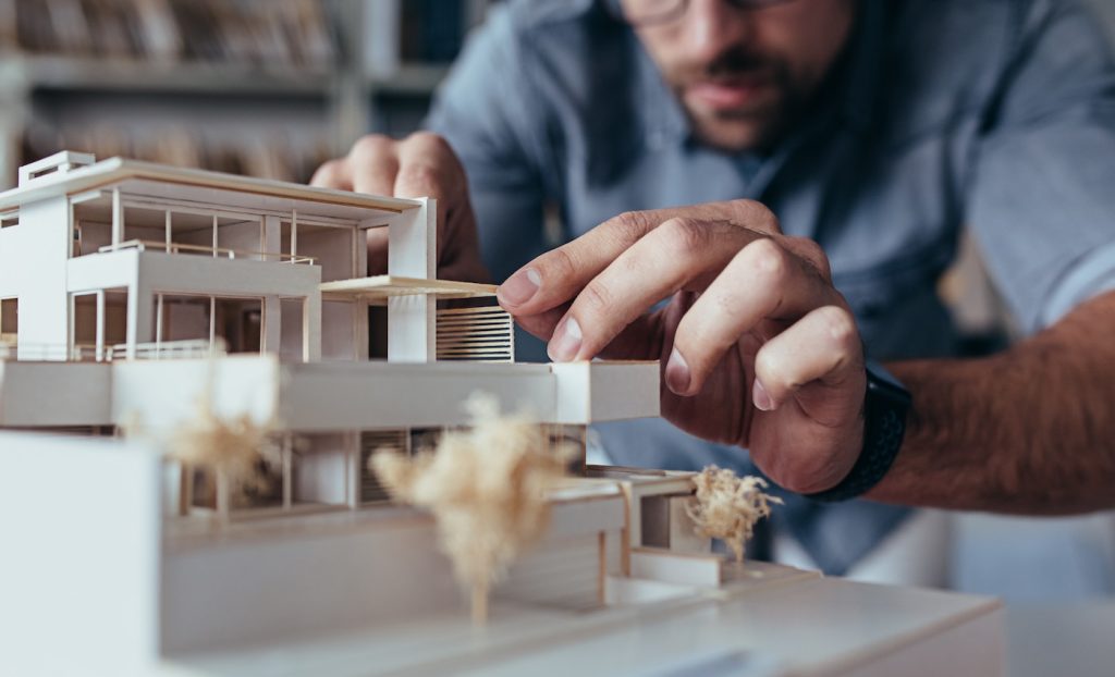 Close up of male architect hands making model house. Man architect working in the office.